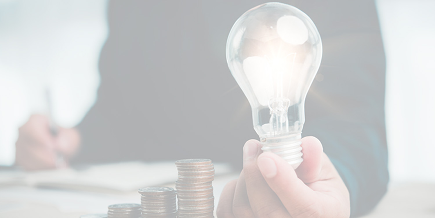 Person holding an illuminated lightbulb above stacked coins, symbolising energy savings